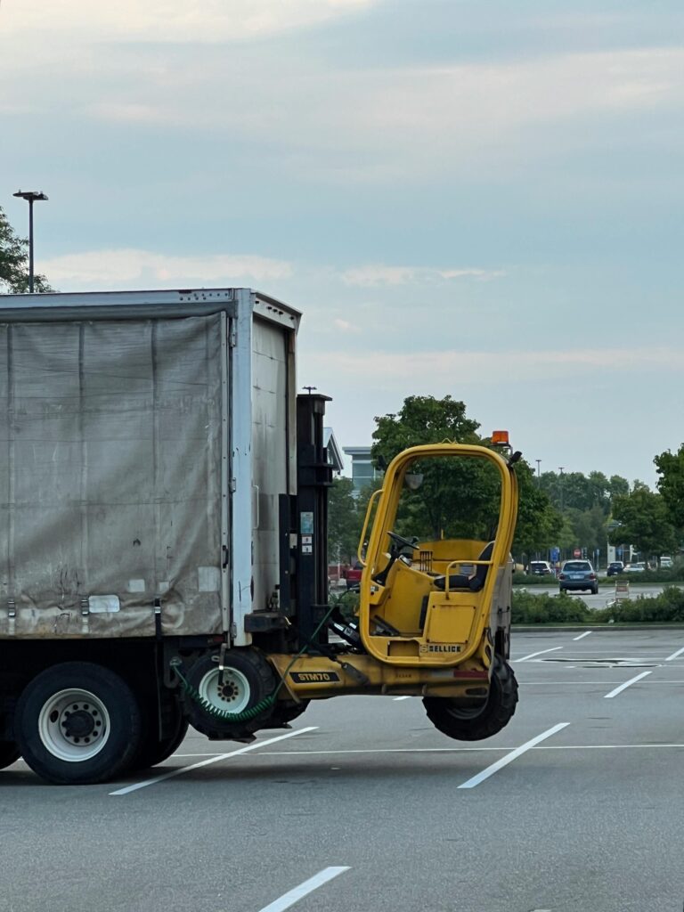 Side view of a truck with a forklift attached, parked in a spacious empty lot.
